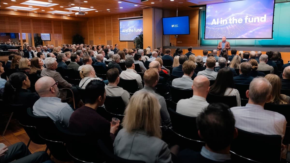 Nicolai Tangen på scenen under NBIMs AI Summit med 'AI in the fund' på skjermen bak ham, foran et fullsatt auditorium